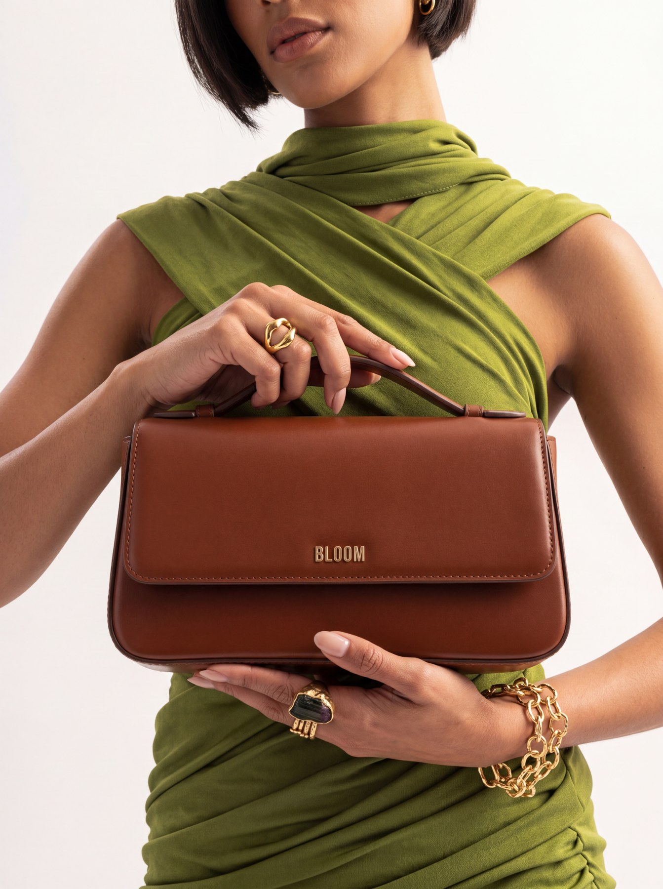 Brown Bloom handbag styled against a green draped dress with gold jewelry.
